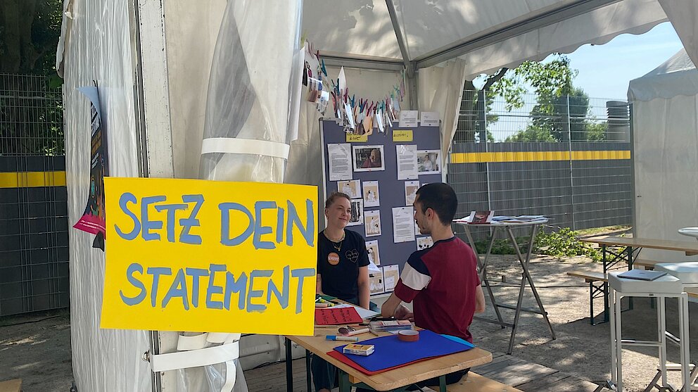 Zelt mit Menschen, die sich unterhalten. ein großes Plakat auf dem steht: Setz dein Statement