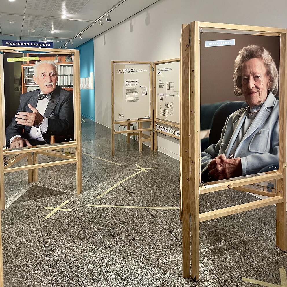 Große Holzrahmen mit Plakaten auf denen Fotos von zwei alten Personen abgebildet sind.