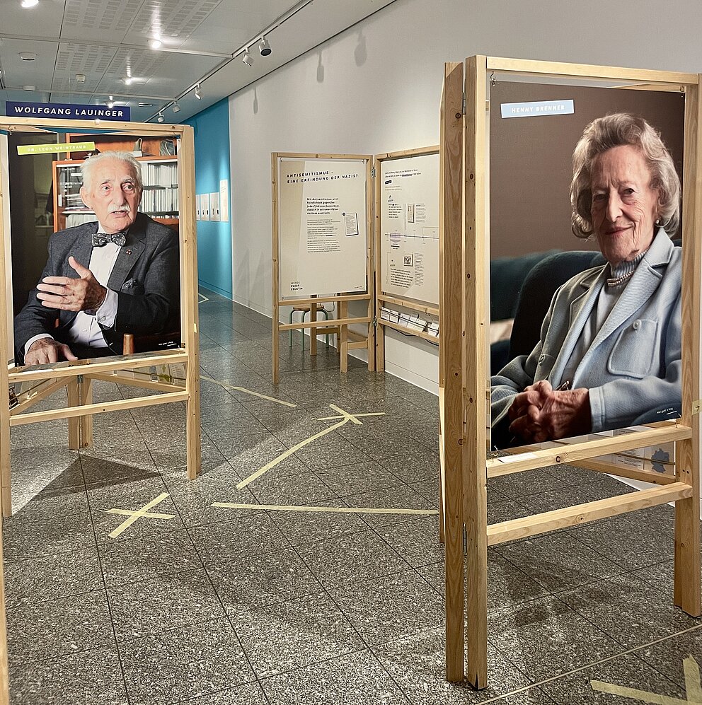 Große Holzrahmen mit Plakaten auf denen Fotos von zwei alten Personen abgebildet sind.