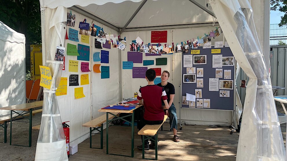 Pavillion mit Wänden voller Plakate und zwei Menschen, die sich unterhalten