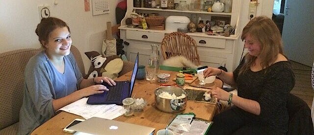 Zwei Frauen sitzen an einem Tisch mit Laptop und vielen Papieren