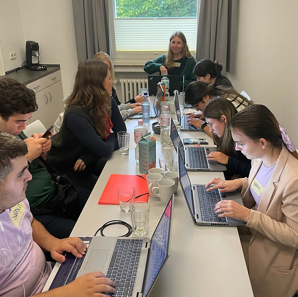 Verschiedene Menschen sitzen an einem Tisch und arbeiten an Laptops.