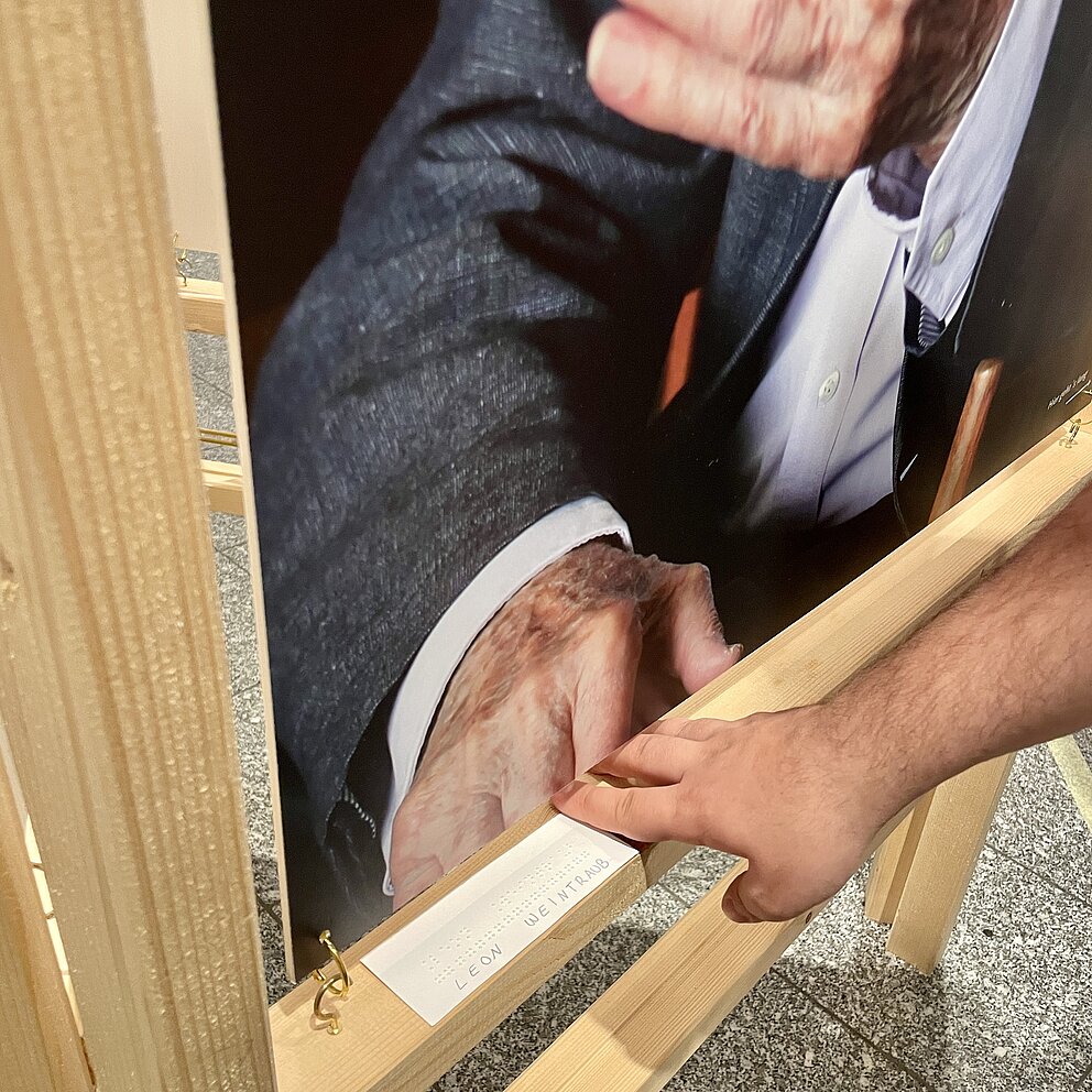 Eine Hand berührt einen Holzrahmen mit einem Plakat