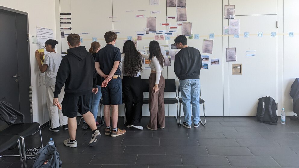 Gruppe Jugendlicher betrachtet Zettel an einer Wand